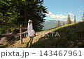 Woman in a white summer dress walks beside a rustic mountain fence, Natural lifestyle scene promotes rural tourism calm leisure and outdoor beauty 143467961
