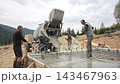 Four workers pour wet concrete from a mixer onto steel rebar flooring, The crew spreads fresh material inside timber forms for a new foundation 143467963