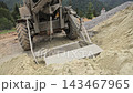 Mobile concrete mixer loader scoops sand beside gravel at a rural site, Heavy equipment gathers building aggregate near a forest construction area 143467965