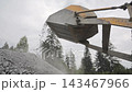 Front loader raises a bucket and drops crushed gravel onto a large pile, Rock aggregate falls from heavy equipment at an outdoor construction site 143467966