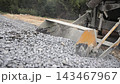 Loader bucket scoops crushed stone from a gravel pile at a work site, Close view of heavy construction machinery gathering aggregate outdoors 143467967