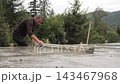 Construction worker screeds fresh concrete across a new foundation slab, A man drags a metal straightedge over the wet surface at an outdoor site 143467968