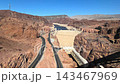 Hoover Dam curves across the Colorado River canyon in Nevada desert, Elevated travel footage reveals roads power facilities and rugged red cliffs 143467969