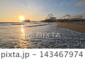 Sunset illuminates Santa Monica Pier above gentle Pacific Ocean waves, Golden coastal footage follows foam washing across a broad sandy shoreline 143467974