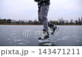 Young man shod in figure skates sliding on ice surface outdoor. Guy skating on frozen river at cloudy day. Sportsman having active leisure at lake in winter cold weather. Close up Slow motion 143471211