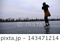 Female skater training rotation skills on frozen river. Young girl shod in figure skates sliding on ice rink outdoor. Sportswoman skating at lake in cold weather. Active leisure at freeze winter day 143471214