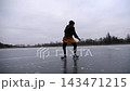 Young girl skating on frozen river at cloudy winter day. Female skater shod in figure skates sliding on ice rink outdoor. Sportswoman training at lake in cold weather. Active leisure at wintertime 143471215