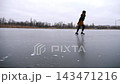 Young girl skating on frozen river at cloudy winter day. Female skater shod in figure skates sliding on ice rink outdoor. Sportswoman training at lake in cold weather. Active leisure at wintertime 143471216