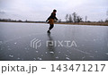 Young girl skating on frozen river at cloudy winter day. Female skater shod in figure skates sliding on ice rink outdoor. Sportswoman training at lake in cold weather. Active leisure at wintertime 143471217
