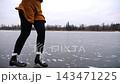 Female skater in figure skates sliding backwards on ice surface outdoor. Girl skating on frozen river at cloudy day. Sportswoman training at lake in cold weather. Active leisure at winter. Slow mo 143471225