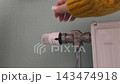 Heating crisis temperature adjustment amidst a heat shortage. A woman in a yellow sweater turns a thermostat dial. Heating season, turning on the heat, cold weather, energy conservation. 143474918