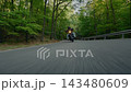 Dynamic tracking shot of a motorcyclist riding through a winding forest road, filmed from the front with fast camera movement, motion blur and a strong sense of speed and adventure. 143480609