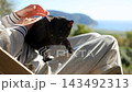 Serene afternoon of woman and black cat relaxing outdoors with sea view 143492313