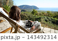 Woman relaxing on deck chair with black cat on lap enjoying coastal sunset 143492314