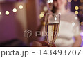 Man approaches young woman with glass of champagne, they clink glasses in decorated Christmas room, POV shot. Cheerful friendly indoor New Year party with sparkling wine 143493707