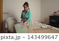 Talented woman meticulously cutting fabric patterns on a table using sharp scissors in her cozy home workshop. 143499647