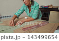 Skilled woman carefully pinning paper sewing patterns onto fabric at a work table in a bright tailoring workshop 143499654