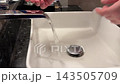 Person Washing Hands Under Running Water in Sink 143505709