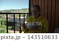 young woman wearing yellow hoodie glasses breakfast terrace country house overlooking mountains. she enjoying nature eating slowly pleasure. background, mountain dotted numerous vacation cottages and 143510633