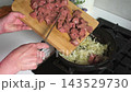 A woman is in the kitchen preparing to fry beef liver. She adds chopped beef liver to sauteed onions already in a pan. The dish includes healthy ingredients like carrots. 143529730
