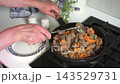 A woman prepares beef liver in a home kitchen. She stirs the liver with sliced carrots and onions in a skillet using cooking oil. The kitchen has a clean, simple layout. 143529731