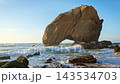 Penedo do Guincho is a large rock arch at Praia da Santa Cruz in Portugal. Waves crash against the rocks as the sun sets over the sandy beach creating a colorful view. 143534703