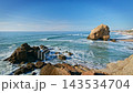Penedo do Guincho stands at Praia da Santa Cruz, Portugal. Waves crash against the sandy beach. The boulder rock arch is a notable feature against the ocean backdrop. 143534704