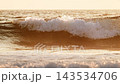 A wave rolls and breaks as the sun sets in Fonte da Telha, Costa da Caparica, Portugal. The scene showcases the beauty of nature in slow motion with a backlit horizon. 143534706