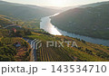 Drone view of the Douro river bend with sunrise reflection, a road with a car and a wine estate among vineyard terraces in Portugal Douro Valley. Push in approach dolly shot. 143534710