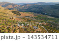 Aerial view of terraced vineyards, farm buildings and a round water reservoir on the hills of the Douro Valley in Portugal in low sunset light. Slide trucking shot. 143534711