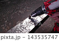 Metal drilling continues on perforated strip. Power drill and abrasive bit move along bright metal while hands steady tool, showing careful workshop fabrication and intense concentration. 143535747