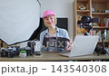 A smiling caucasian woman wearing a pink cap presents a black box to the camera in her home studio setup with professional equipment A smiling caucasian woman wearing a pink cap presents a black box to the camera in her home studio setup with professional equipment 143540308