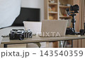 A desk is set up with professional videography equipment including cameras, lenses, a gimbal, and a laptop for editing 143540359