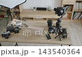 A collection of modern and vintage cameras, lenses, a gimbal, headphones, and a laptop are arranged on a wooden table for content creation 143540364