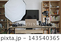 A home photography studio setup with cameras, lighting, and a laptop on a desk, with bookshelves in the background 143540365