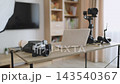 A desk is set up with various photography equipment including cameras, a laptop, and lighting for content creation 143540367