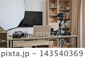 A collection of cameras, lenses, a gimbal, and a softbox are arranged on a desk with a laptop and smartphone, ready for creative work 143540369