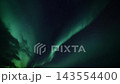 Luminous green aurora borealis ribbons sweeping across starry night sky with clouds for depth and contrast, flowing celestial motion captured from wide viewpoint, tranquil atmospheric landscape scene 143554400