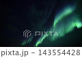 Green aurora borealis ribbons sweeping across starry night sky with flowing vertical and diagonal light bands, serene polar landscape scene viewed from dark horizon at night 143554428