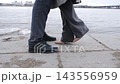 Cropped low angle view of a man and woman standing close together on a riverside promenade, showing black leather boots and elegant pale pink high heels. Concept of dating, relationships, fashion 143556959