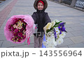 child holding bouquet of flowers on outdoor walkway with tiled pavement and barriers, calm and content moment with pink wrapping paper and dark clothing material. 143556964