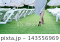 woman in white dress walking on grass in calm and serene outdoor lawn with lounge chairs and umbrellas, wedding photography, beach resort scenes, commercial natural light, clean background. 143556969