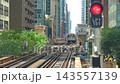 Elevated railway tracks stretch through a dense city center surrounded by tall modern buildings. A train moves forward along complex rail lines in an urban transportation network. 143557139