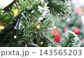 Snow covered pine tree branches with twinkling Christmas lights and red ornament 143565203