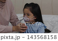 mother giving respiratory treatment with nebulizer mask to sick preschool child girl in a bed 143568158