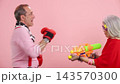Playful senior couple fighting with toys on a pink background 143570300