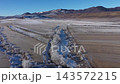 Aerial view of snow-covered field dotted with hay bales under a clear blue sky in a mountainous region during winter 143572215