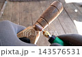Gloved craftsman sands a wooden tool handle with a rotary multitool and cone shaped abrasive bit outdoors on a sunlit porch deck 143576531