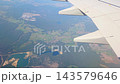 Airplane wing viewed from above as flight passes over winding rivers, forests, farmland, fields, and scattered rural settlements across a colorful landscape from the sky 143579646
