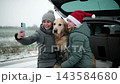 Happy Mother And Daughter Wearing Santa Hats Take A Selfie With Dog In A Car Trunk During A Winter Road Rest Stop 143584680